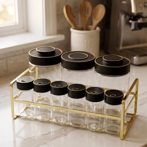 9-piece luxury glass spice jars with black gold-accented lids stored on a metallic gold wire rack on a marble kitchen countertop.