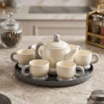 Ceramic rotating tray tea set with six cups and a kettle arranged neatly on a modern kitchen countertop.