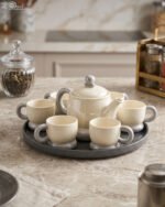Ceramic rotating tray tea set with six cups and a kettle arranged neatly on a modern kitchen countertop.