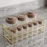 A 9-piece glass spice jar set with matte brown lids and gold-tone metal rack sitting on a granite countertop.