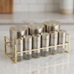 9-piece brushed stainless steel and glass spice jar set with gold rim accents arranged on a gold metal countertop rack