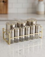 9-piece brushed stainless steel and glass spice jar set with gold rim accents arranged on a gold metal countertop rack
