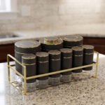 9-piece matte black and gold luxury spice rack set with clear glass bottoms on a granite countertop.