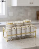 9-piece white ceramic and clear glass spice jar set with gold accents arranged in a gold metal rack on a marble countertop