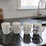 Set of 4 ceramic coffee mugs with blue and grey plaid grid patterns displayed on a kitchen countertop.
