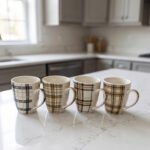 Set of four modern plaid ceramic coffee mugs displayed on a white marble kitchen countertop.