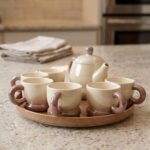 Beige and brown ceramic tea set with 6 cups, a teapot, and a rotating tray arranged on a kitchen counter