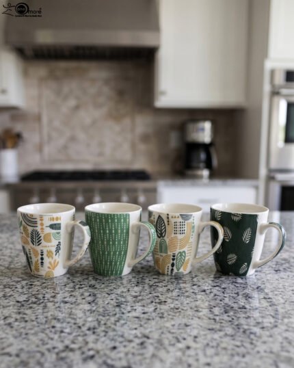 Four ceramic coffee cups featuring green, yellow, and beige geometric and botanical patterns lined up on a granite kitchen countertop