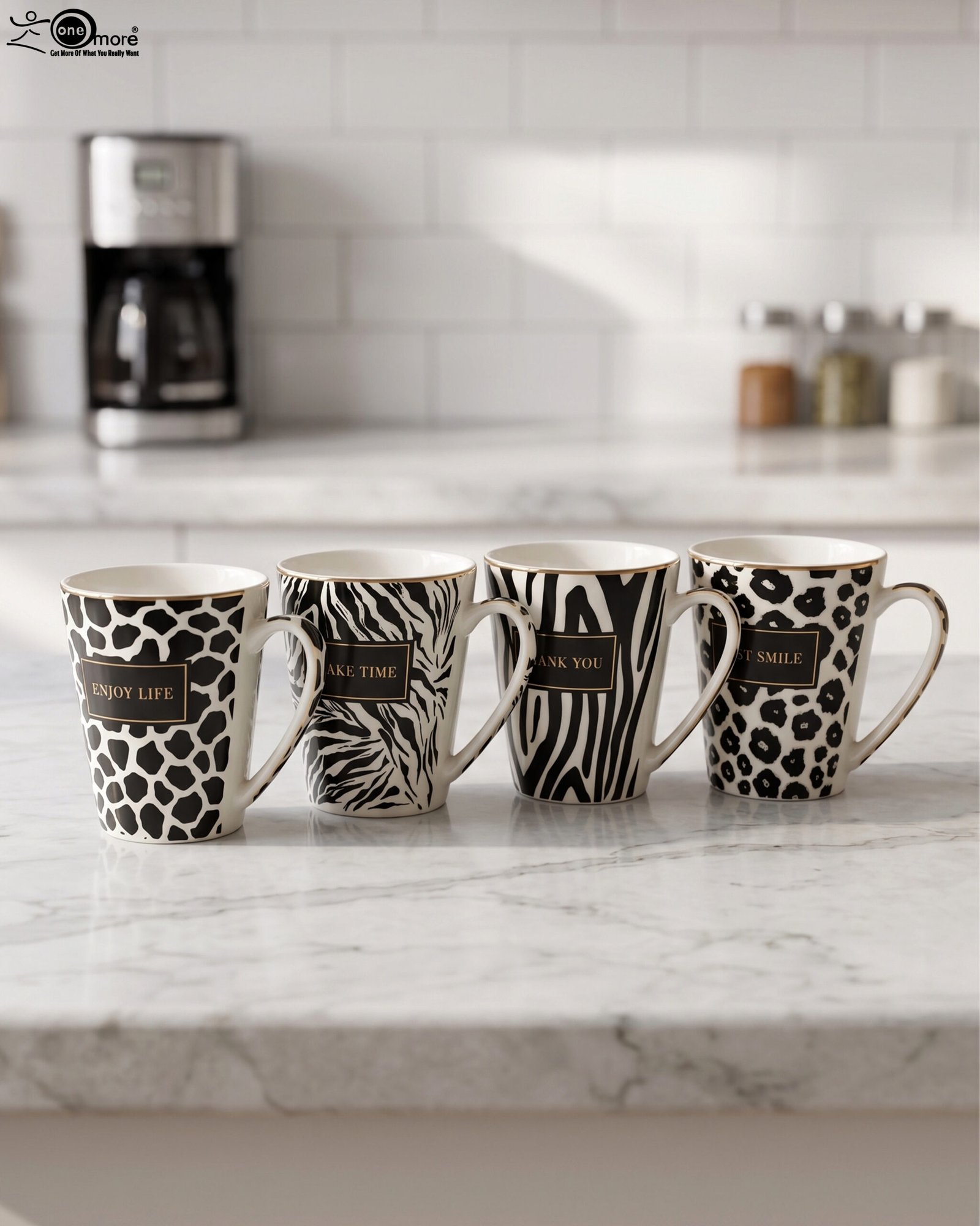1 Set of four modern ceramic coffee mugs featuring black and white giraffe, zebra, and leopard prints with gold trim sitting on a marble kitchen counter.