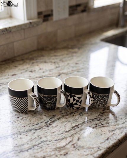 Set of four modern ceramic coffee mugs featuring black and white geometric patterns lined up on a granite countertop.