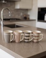 Four ceramic coffee cups with vertical and horizontal striped patterns lined up on a kitchen counter