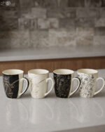 Set of 4 OneMore ceramic coffee mugs featuring abstract face line art in black, white, and gold on a kitchen countertop.