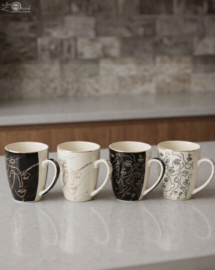 Set of 4 OneMore ceramic coffee mugs featuring abstract face line art in black, white, and gold on a kitchen countertop.