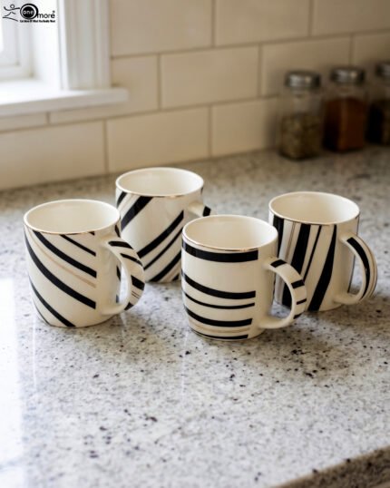 Set of 4 white ceramic coffee mugs featuring modern black stripes and subtle gold rim accents sitting on a granite kitchen countertop.