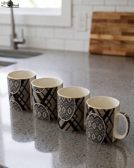 4-piece ceramic coffee mug set with black and grey geometric tribal patterns and gold rims lined up on a granite kitchen countertop
