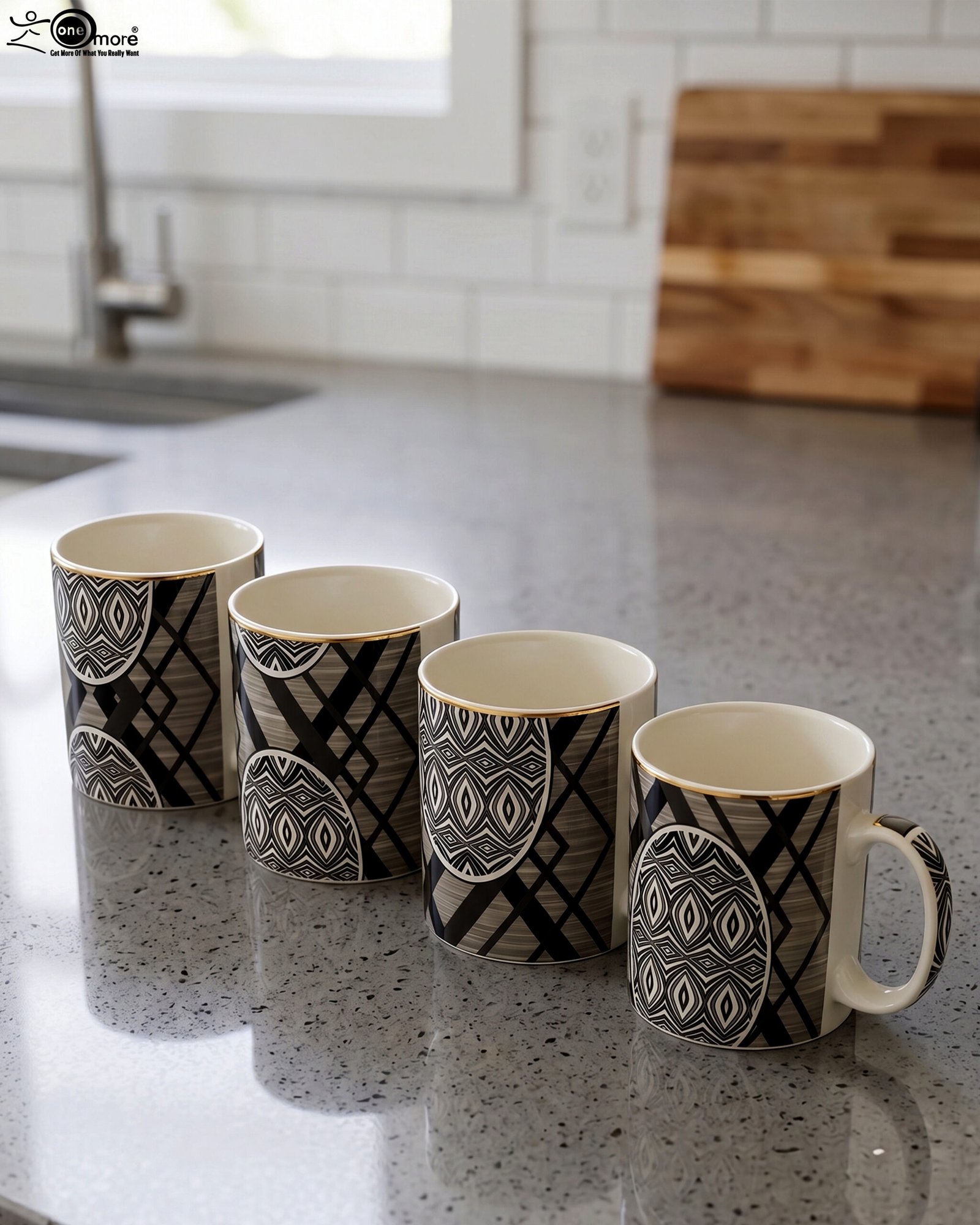 1 4-piece ceramic coffee mug set with black and grey geometric tribal patterns and gold rims lined up on a granite kitchen countertop