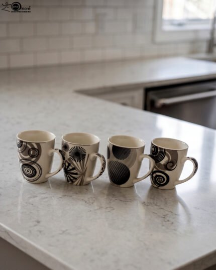 Set of 4 cream ceramic coffee mugs with distinct black geometric and swirl patterns displayed on a white marble countertop