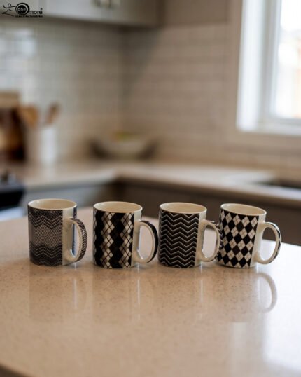 Four-piece modern black and white ceramic coffee mug set with geometric chevron and argyle patterns lined up on a kitchen counter.