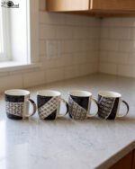 Set of 4 modern ceramic coffee mugs with distinct black, white, and grey geometric patterns displayed on a kitchen countertop.