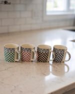 Four ceramic coffee mugs with gingham and polka dot patterns lined up on a marble countertop