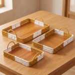 Set of three rectangular handwoven rattan serving trays with wooden bases and handles on a wooden table.