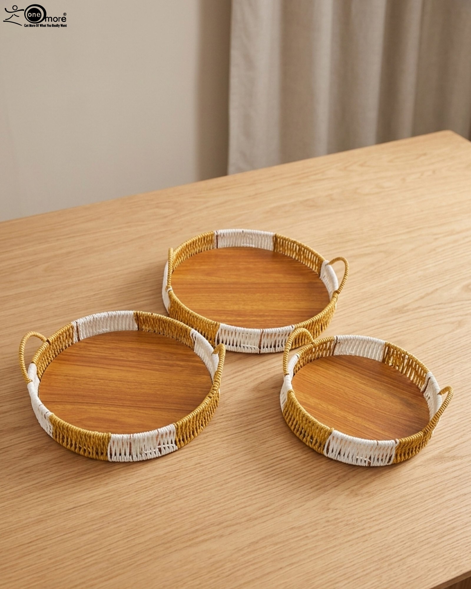 1 Three-piece round handwoven rattan serving tray set with white and tan woven edges and wooden bases on a light wood table.