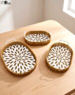 Set of 3 oval woven rattan serving trays with white handles and a modern geometric floral pattern base resting on a wooden table.