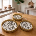 Set of 3 round handwoven rattan serving trays with white base patterns and handles resting on a wooden table