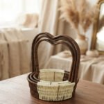Nested set of three brown and cream woven rattan baskets with heart-shaped arch handles on a wooden table.