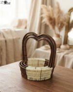 Nested set of three brown and cream woven rattan baskets with heart-shaped arch handles on a wooden table.