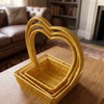 Set of 3 yellow woven rattan nesting trays with high arched handles stacked on a wooden coffee table.