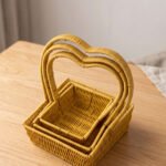 Three yellow handwoven rattan baskets nested together featuring prominent heart-shaped top handles on a wooden table.