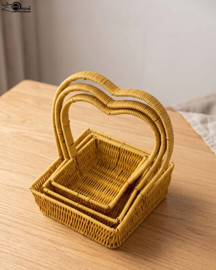Three yellow handwoven rattan baskets nested together featuring prominent heart-shaped top handles on a wooden table.