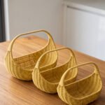 Three yellow handwoven rattan baskets with arch handles nested in a row on a wooden table