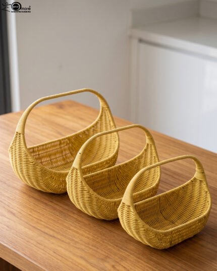Three yellow handwoven rattan baskets with arch handles nested in a row on a wooden table