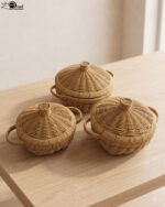 3-piece handwoven natural rattan basket set with fitted lids and side handles sitting on a light wooden table