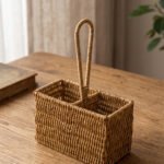 Handwoven rattan spoon holder basket with center handle and two compartments on a wooden table.