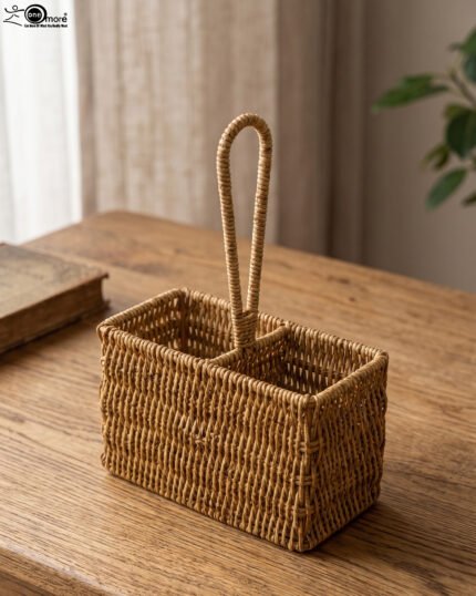 Handwoven rattan spoon holder basket with center handle and two compartments on a wooden table.