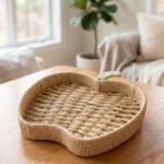 Handwoven apple-shaped natural rattan fruit dish sitting on a wooden coffee table in a modern living room setting.