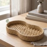 Handwoven pear-shaped rattan fruit dish resting on a light wooden table next to stacked decorative books and a small white vase.