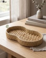 Handwoven pear-shaped rattan fruit dish resting on a light wooden table next to stacked decorative books and a small white vase.