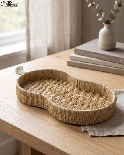 Handwoven pear-shaped rattan fruit dish resting on a light wooden table next to stacked decorative books and a small white vase.