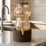 3.2L fluted amber glass beverage dispenser with wooden lid, wooden base, and gold spigot on a kitchen counter