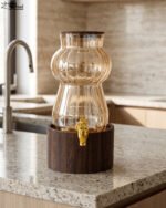 3.2L fluted amber glass beverage dispenser with wooden lid, wooden base, and gold spigot on a kitchen counter