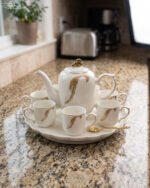 White and gold ceramic tea set with 6 cups, 1 kettle, and a rotating tray displayed on a kitchen counter.