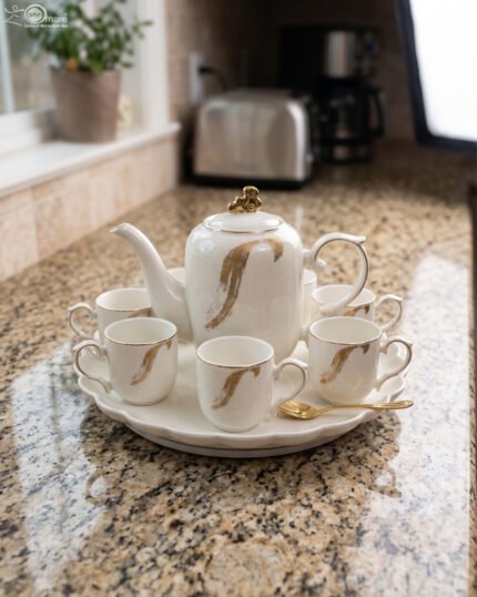 White and gold ceramic tea set with 6 cups, 1 kettle, and a rotating tray displayed on a kitchen counter.