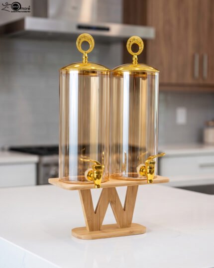Dual 3.3L amber shaded glass beverage dispensers with gold lids and spigots on a W-shaped wooden stand sitting on a modern kitchen counter.
