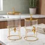 Two luxury clear glass beverage dispensers with gold deer lid handles and matching metallic stands on a marble countertop