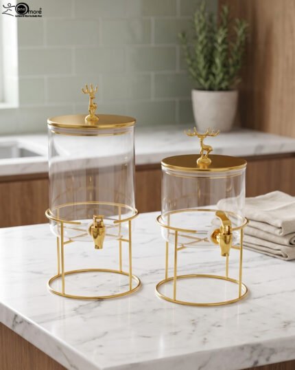 Two luxury clear glass beverage dispensers with gold deer lid handles and matching metallic stands on a marble countertop