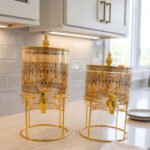 Amber tinted glass beverage dispenser with intricate Islamic mosque gold pattern on a metal stand.